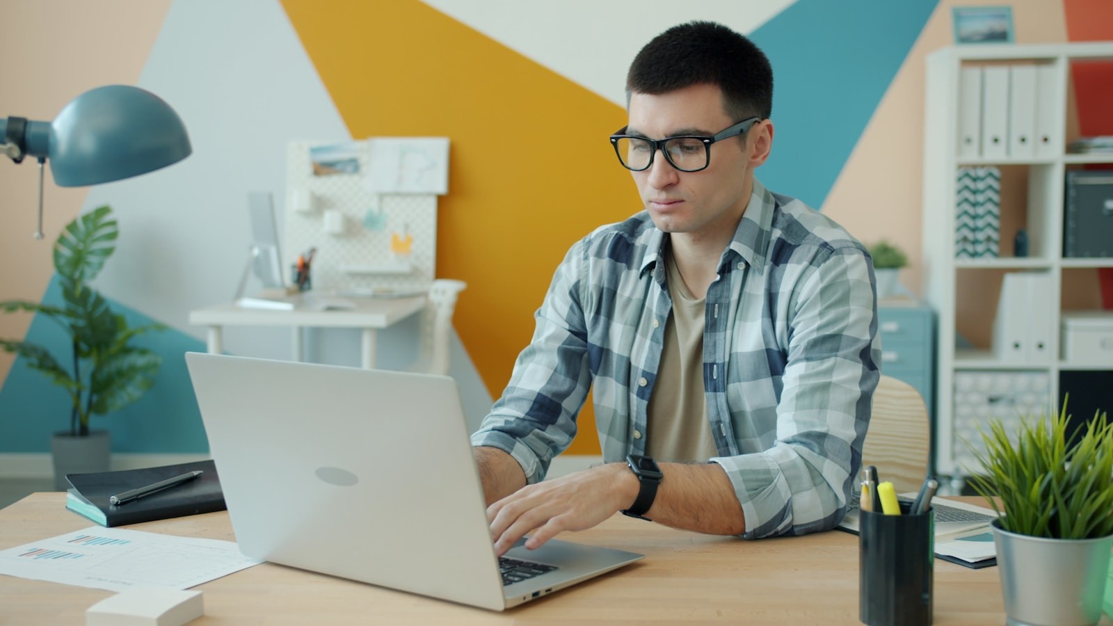 A developer with glasses typing on a laptop at a modern desk, representing how an AI gateway and an API gateway both mediate traffic between applications and backends