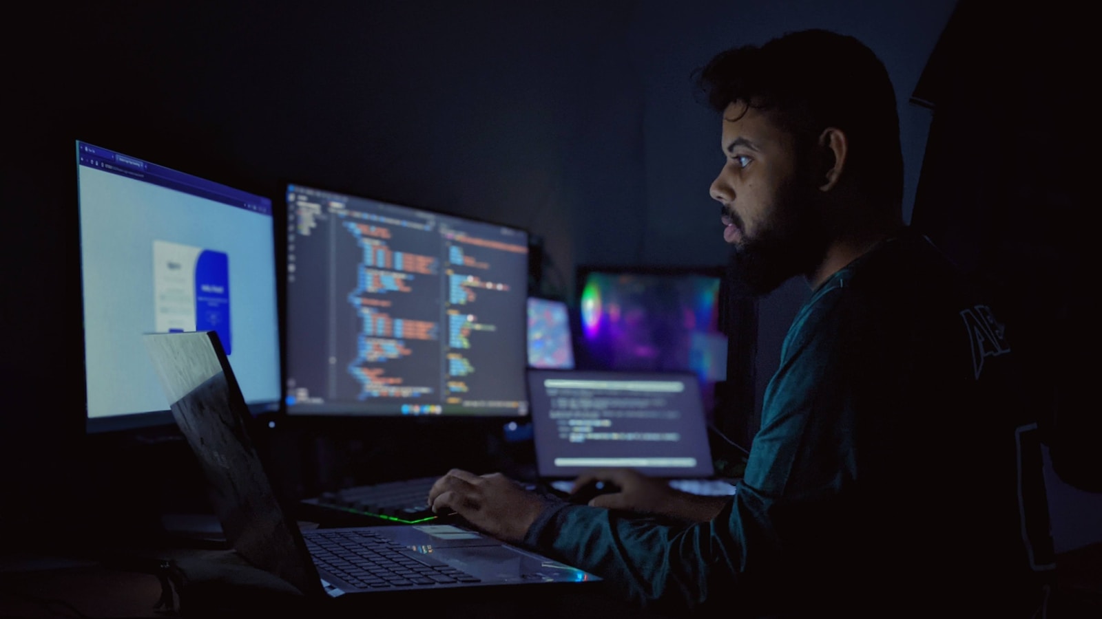 A developer at a dark desk facing three computer monitors, one workspace that reaches several applications at once, illustrating unified access in an LLM gateway guide